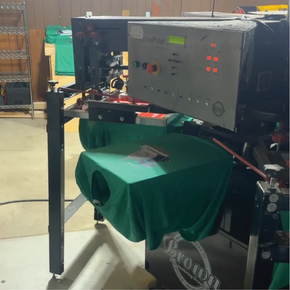 Automatic screen printing press mid-run on a green t-shirt in the shop
