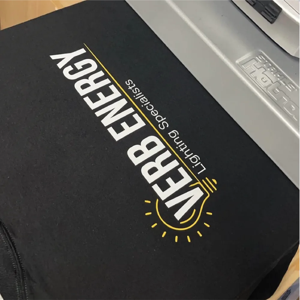 Black business tee with the Verb Energy lighting specialists logo on a heat press