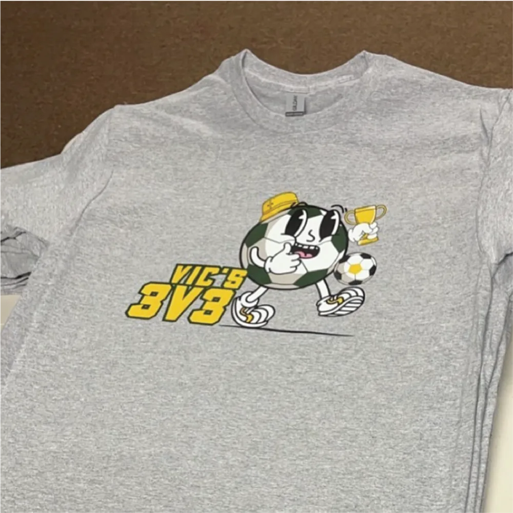 Grey event tee with a full-color Vic's 3v3 soccer mascot graphic
