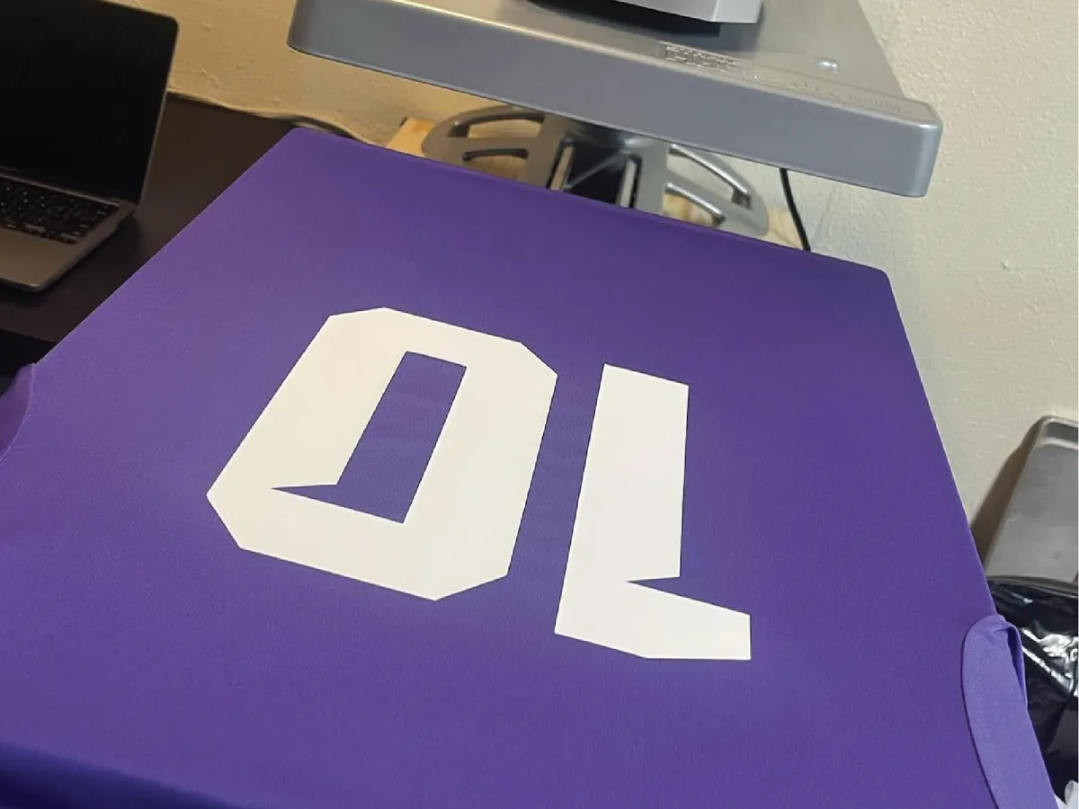 Heat press applying a vibrant full-color lion graphic transfer onto a navy t-shirt in a print shop
